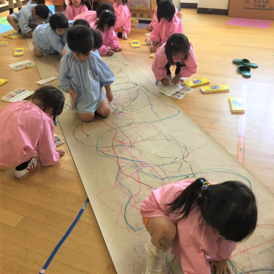 壁や床の画用紙に夢中で絵を描く子どもたち。