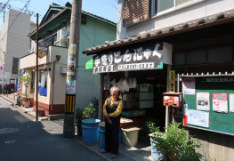 大正13年築（102年前）の狭川商店は入母屋作りの銅板張りです。「手作りこんにゃく」の黒い看板も狭川さんの手作りです。お隣の床屋も狭川商店と同じ作りで狭川さんの祖父の代から続いています。昔はこの通りも賑やかな商店街だったそうです。戦中には近くの「日本アルミ」工場を狙い爆撃があったそうですが、爆弾は北に逸れて狭川商店の一角は焼け残ったそうです
