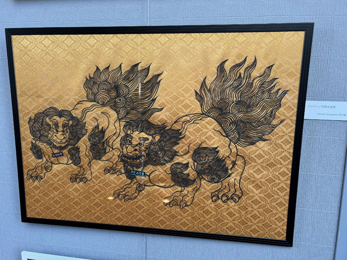 《シーサー／狩野永徳風》  2024  A2  –  コラボレーションにあたり、シーサーというオーダーを受けて切り絵をつくったことをきっかけに展開した個人作品。狩野永徳作《唐獅子図屏風》を翻案し、二対の力強いシーサーがLove & Peaceを掲げている