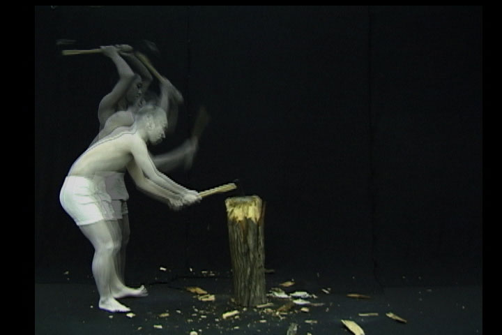 《破壊←↓→創造》 1999 映像 7分 – 石原さんの学部時代の作品。半裸の真っ⽩い⼈影が⽊を削っていく。その姿は時に巻き戻され、時に早送られ、時に重なる。美術館に⽊を置き、来場した観客が削ることによって完成するネオダダの作品のオマージュでありながら、ネオダダに対するさらなるネオイズムのかたちをとった価値再構成の試み